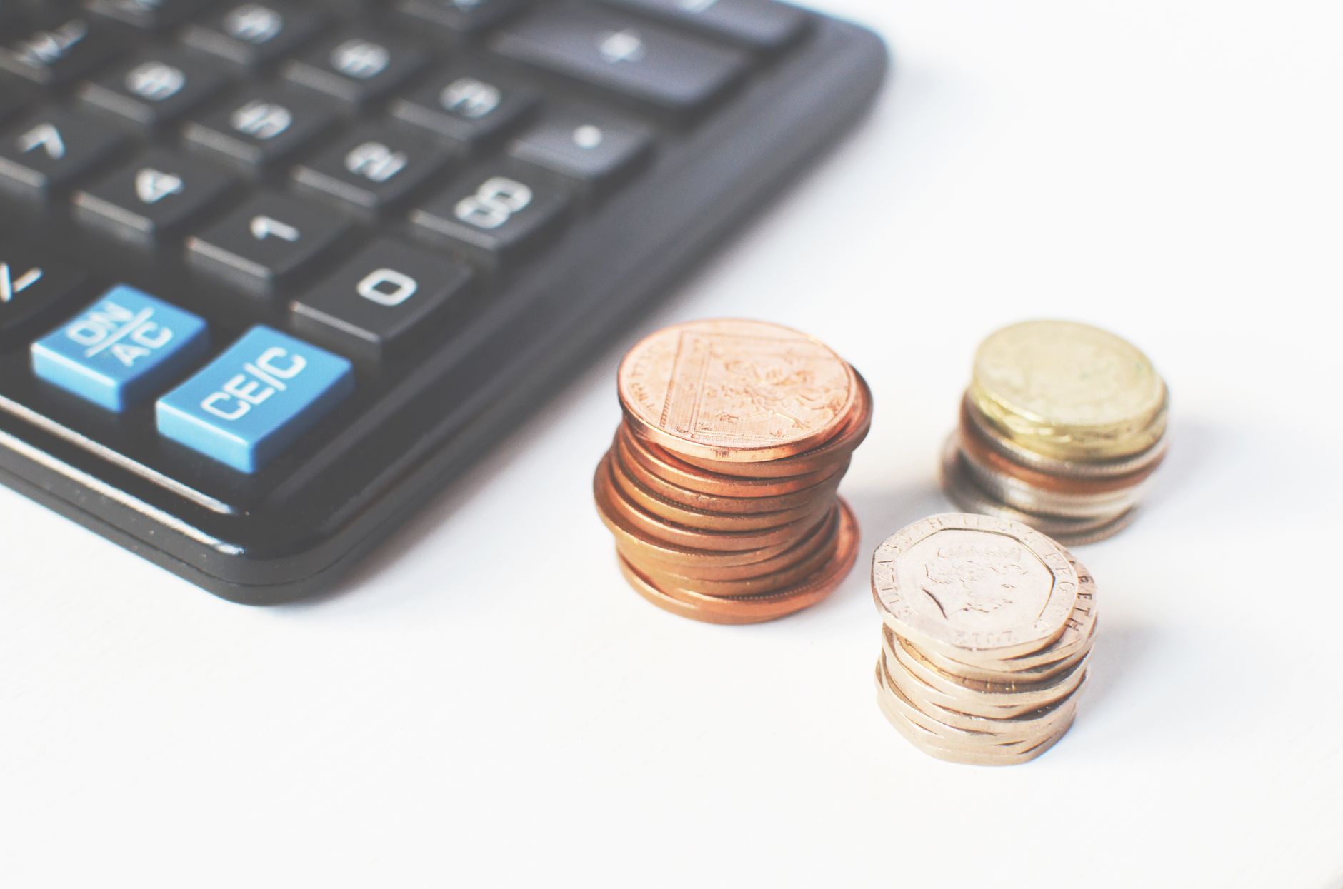Stacks of British coins beside a calculator on a white desk