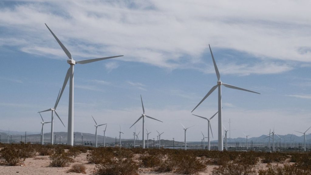 Investors stay committed to climate goals despite policy uncertainty Multiple white wind turbines in a desert landscape with sparse vegetation and mountains in the distance under a cloudy sky